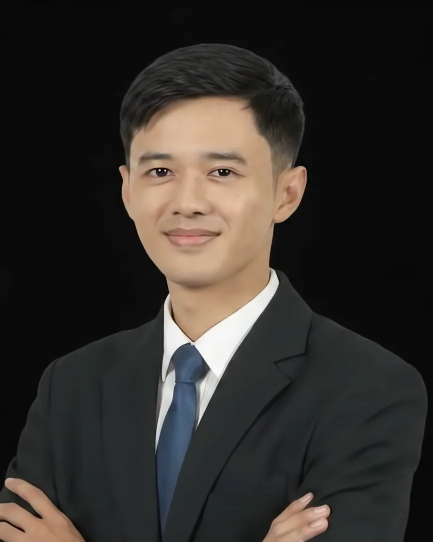 Radhian, in a dark suit and blue tie, arms crossed, smiling